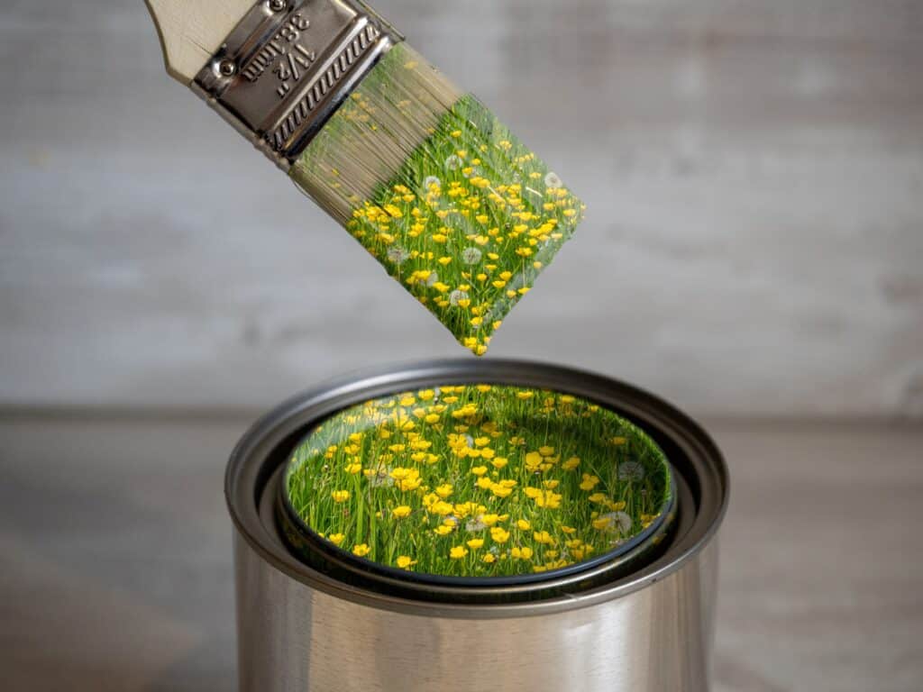 eco-friendly paint brush and bucket with yellow flowers and green grass inside the paint and on the brush 