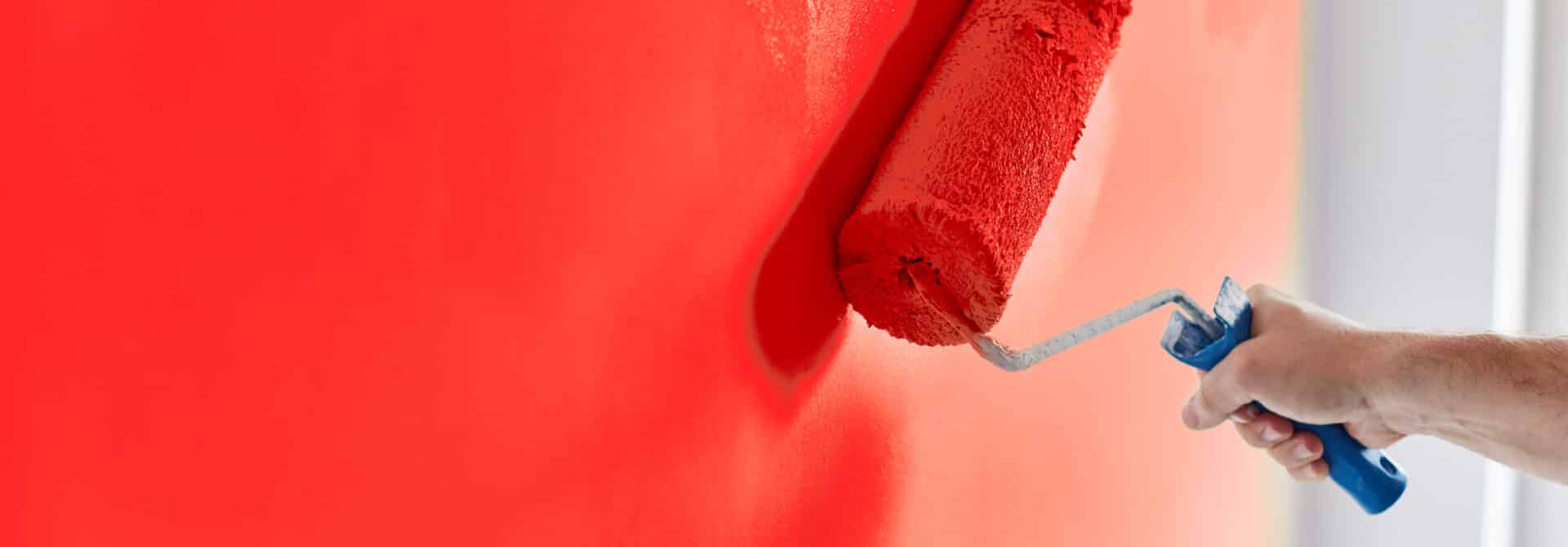 hand painting a wall red with a roller brush
