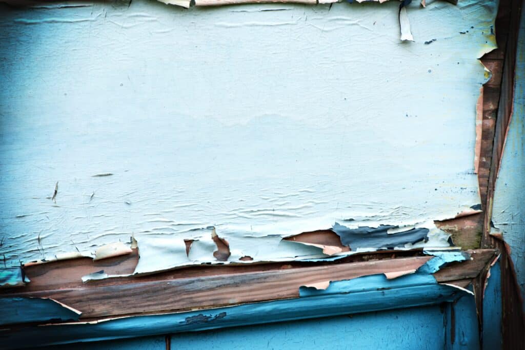 white and blue paint peeling off wood exterior of a home