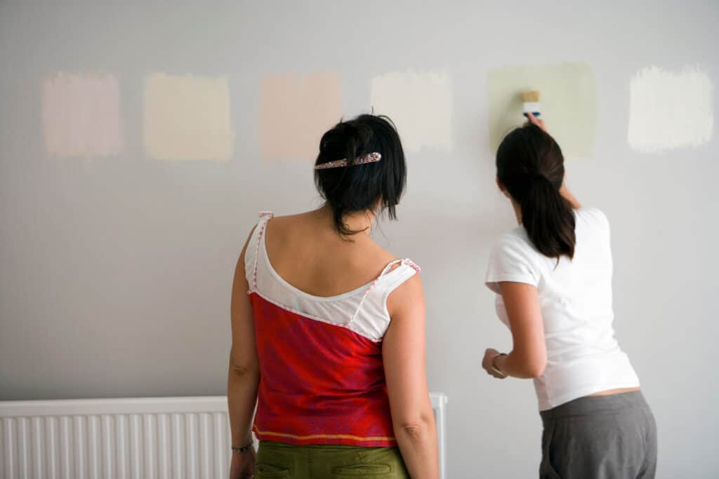 2 women painting paint sample swatches on a wall 