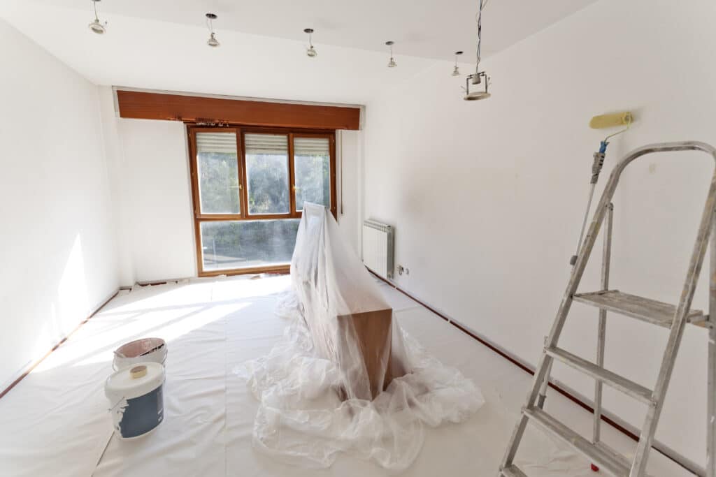 a white room with brown window pane being prepared for painting with plastic covering floors and furniture