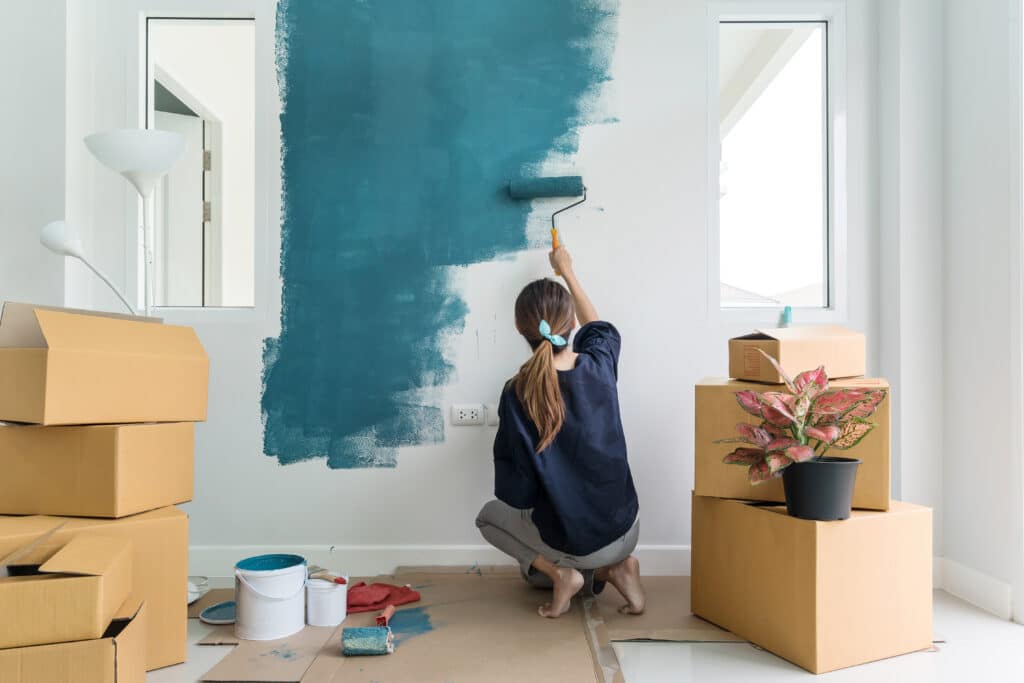 Young asian happy woman painting interior wall of apartment 