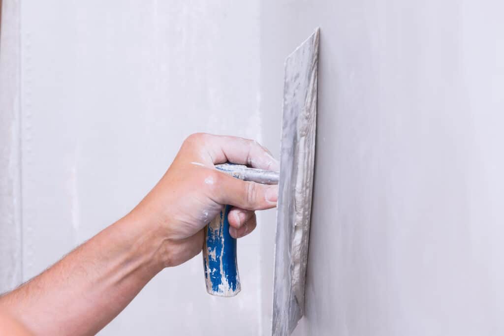 white persons hand holding a flat scraping paint tool made for skim coating